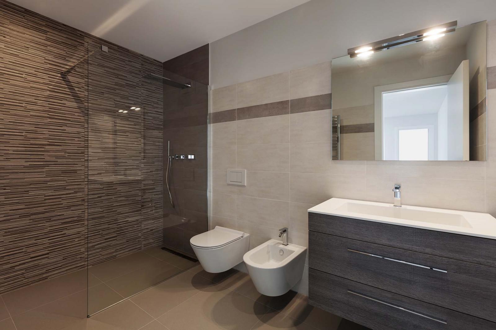 Nhà vệ sinh màu trắng xen kẽ mảng tường nâu, gương treo tường, vách kính phân riêng phòng tắm.